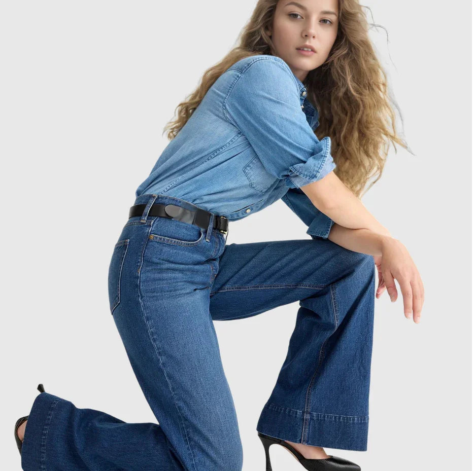 Woman wearing rolled-up denim shirt and wide-leg jeans with black belt and heels on light background