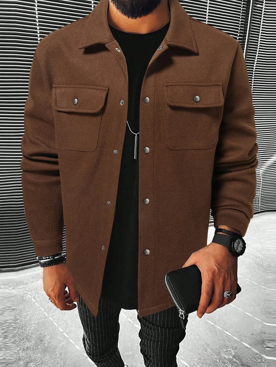 Man wearing brown button-up jacket with flap pockets, black shirt, striped pants, and holding black wallet