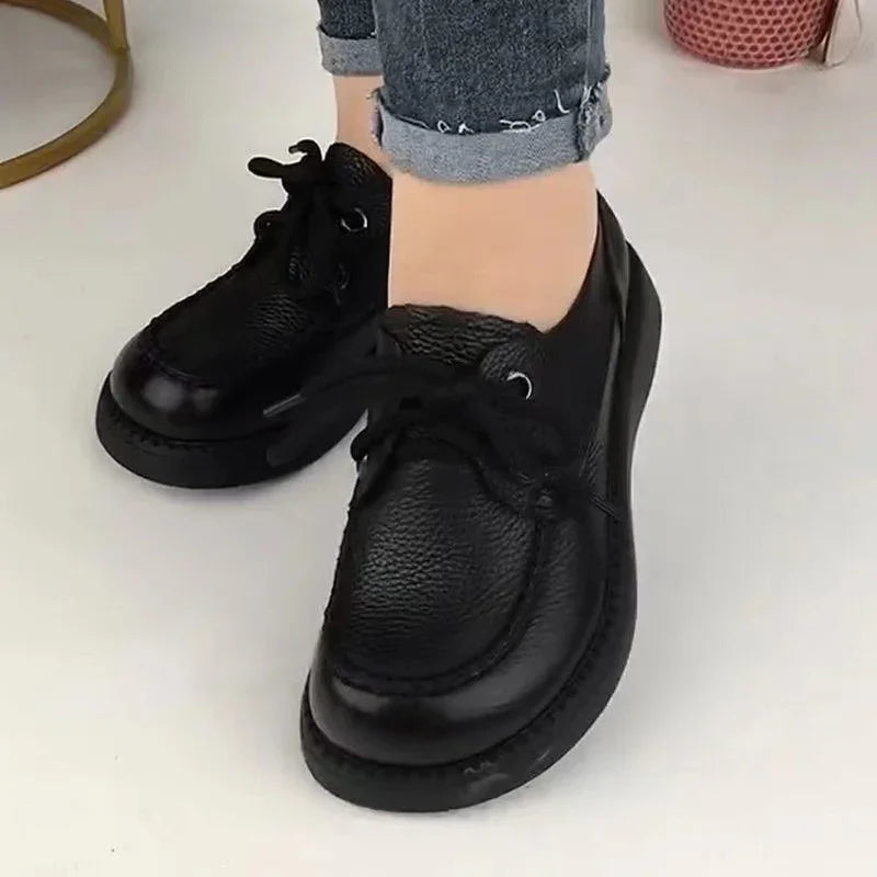 Close-up of black leather lace-up shoes worn with cuffed blue jeans on white floor