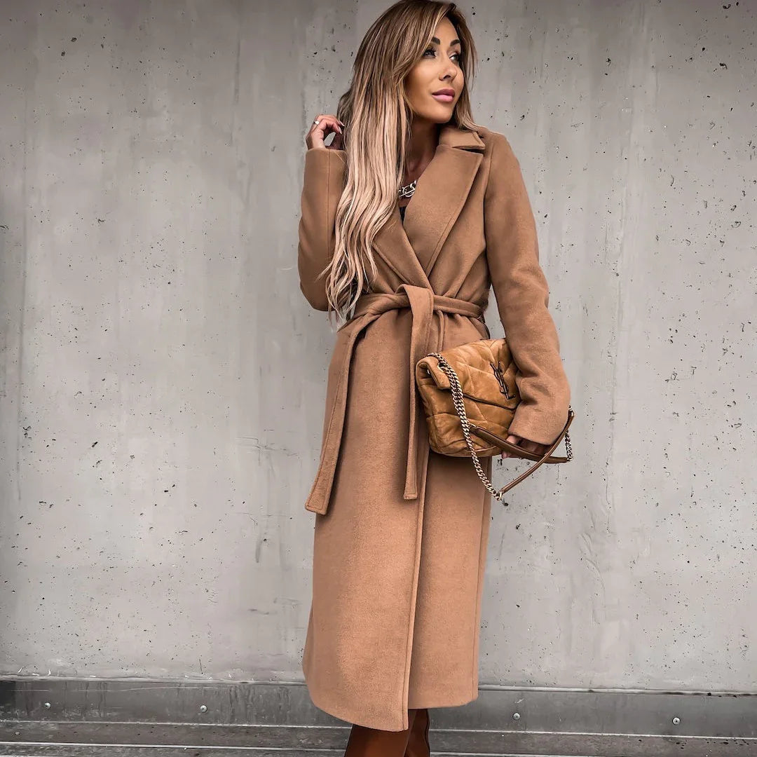 Woman wearing a long camel-colored belted coat holding a tan quilted Yves Saint Laurent handbag