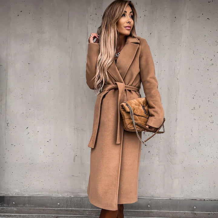 Woman wearing a long camel-colored belted coat holding a tan quilted Yves Saint Laurent handbag
