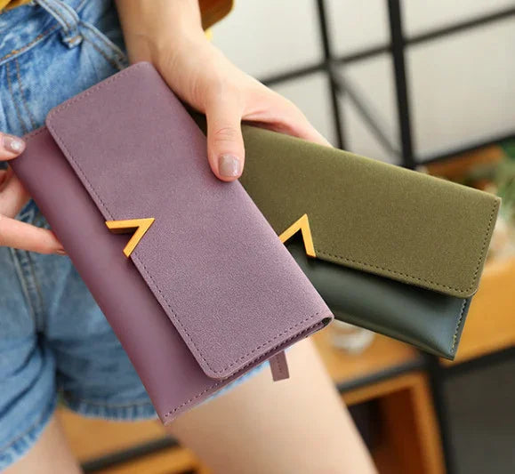 Woman holding two stylish wallets in purple and green with gold V-shaped clasps, casual outfit