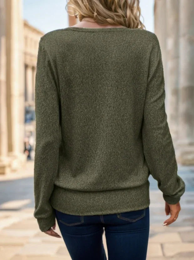 Woman wearing olive green long-sleeve sweater and dark blue jeans walking outdoors in urban setting