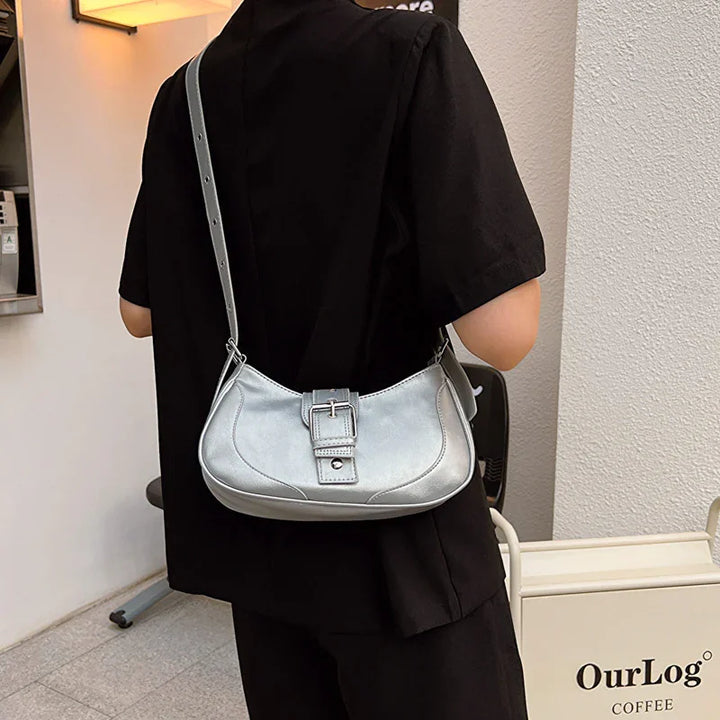 Person wearing black outfit carrying a silver leather shoulder bag with buckle detail
