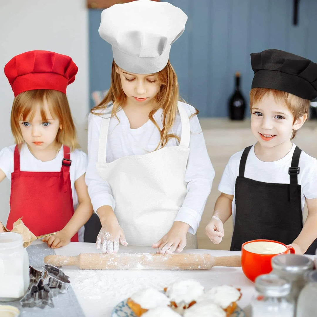 Three children in red, white, and black chef hats and aprons baking with rolling pin and dough