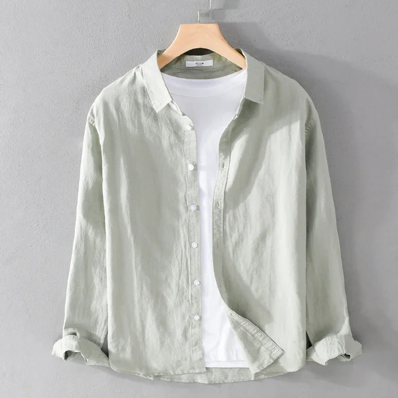Light green linen button-up shirt over white t-shirt on wooden hanger against gray wall