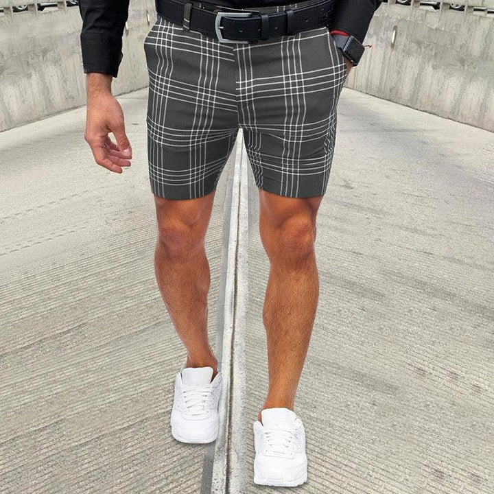 Man wearing black and white plaid shorts with black belt, black shirt, white sneakers, and smartwatch on concrete path