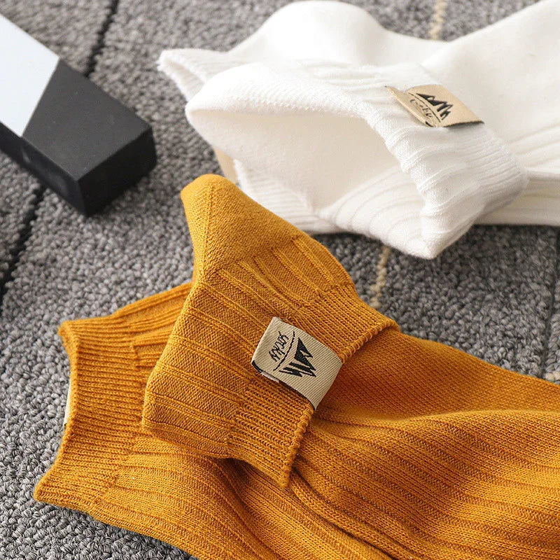Close-up of mustard yellow and white ribbed knit socks with logo tags on gray textured surface