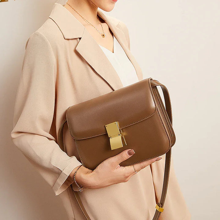 Woman wearing beige blazer holding brown leather crossbody bag with gold clasp