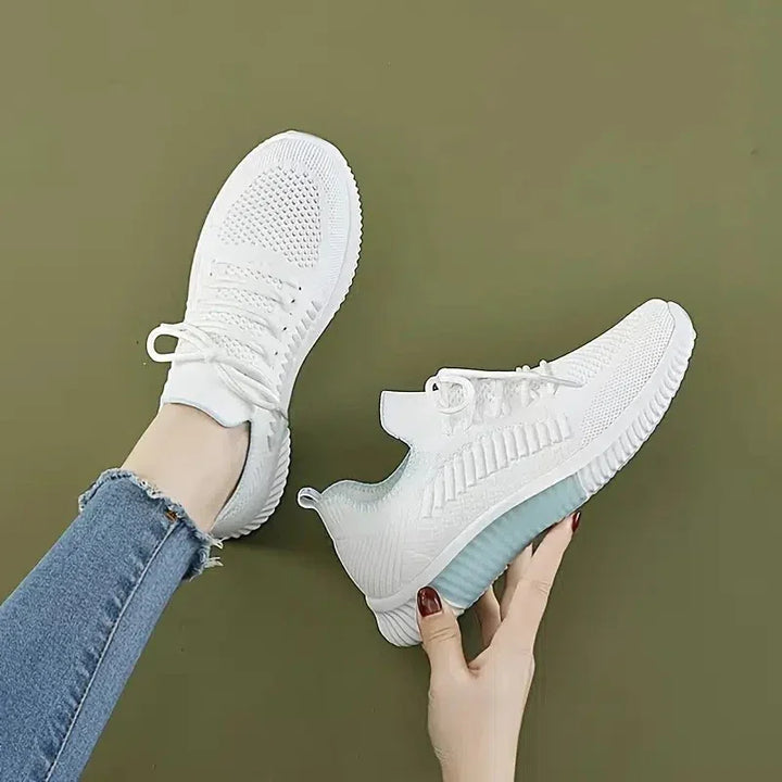 White knitted sneakers with blue cushioned soles worn and held by hands against olive green background