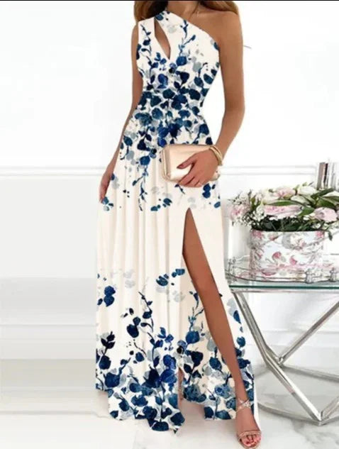 Woman in white one-shoulder floral maxi dress with blue flowers and a thigh-high slit, holding a beige clutch