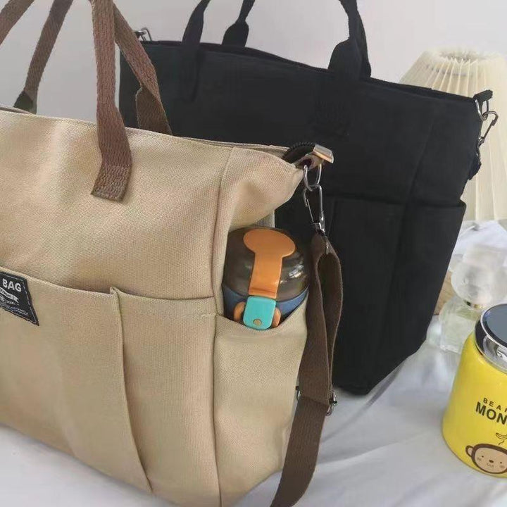 Beige and black canvas tote bags with side pocket holding a reusable water bottle on white surface