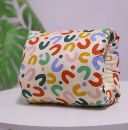 Folded colorful abstract patterned fabric pouch on white surface with green leaf background