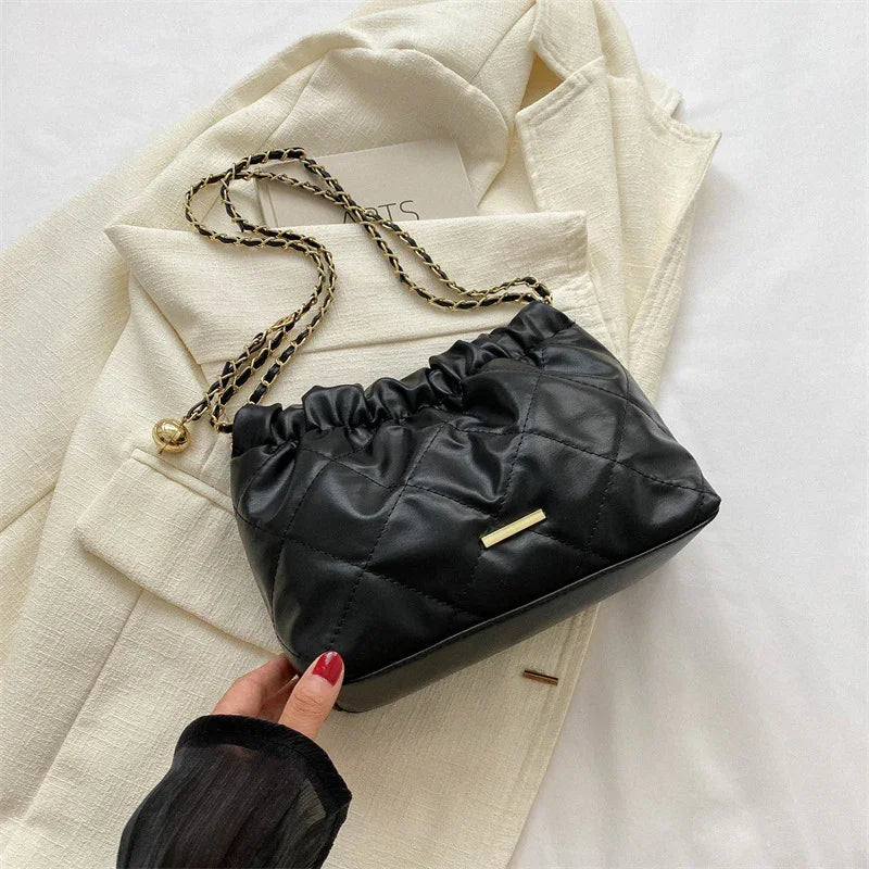 Black quilted leather handbag with gold chain strap on cream blazer with red nail polish hand
