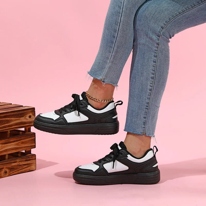 Person wearing black and white sneakers with blue jeans and a gold ankle bracelet on a pink background