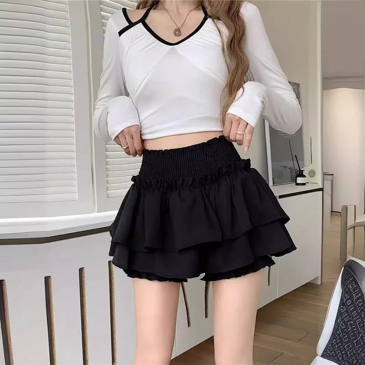 woman wearing white long-sleeve crop top and black layered ruffle skirt shorts indoors