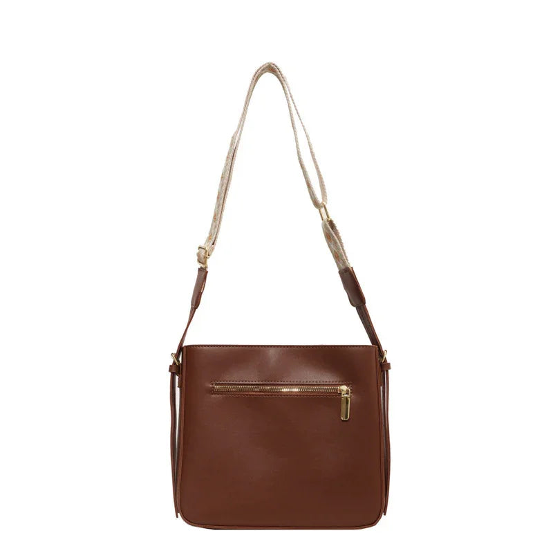 Brown leather crossbody bag with front zipper pocket and adjustable beige strap on white background