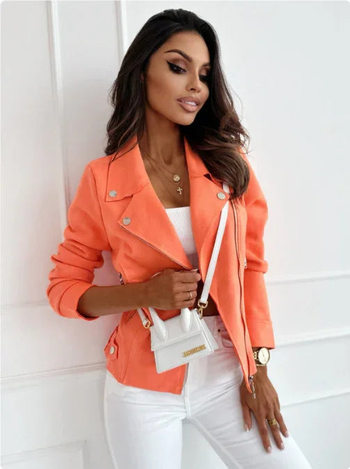 woman wearing bright orange jacket and white pants holding small white designer handbag against white wall