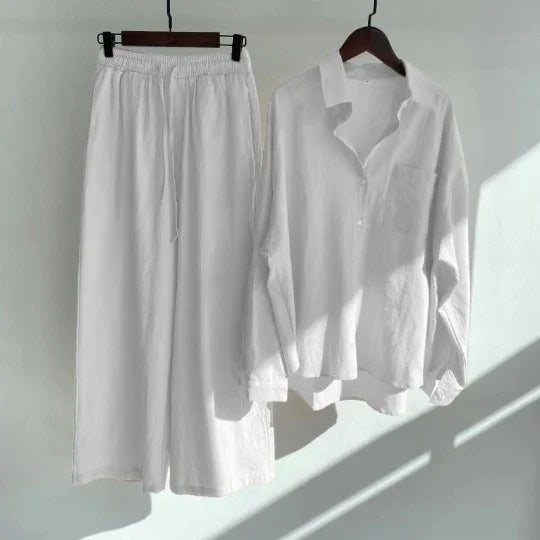 White linen long sleeve shirt and wide leg pants set hanging on wooden hangers in sunlight