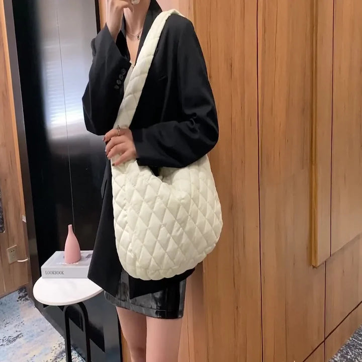 Woman wearing black blazer and leather skirt carrying a white quilted shoulder bag indoors