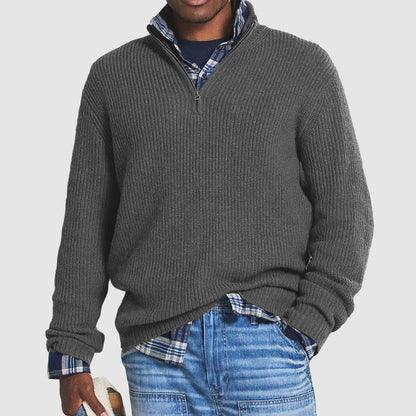 Man wearing a gray ribbed quarter-zip sweater over a blue plaid shirt and blue jeans
