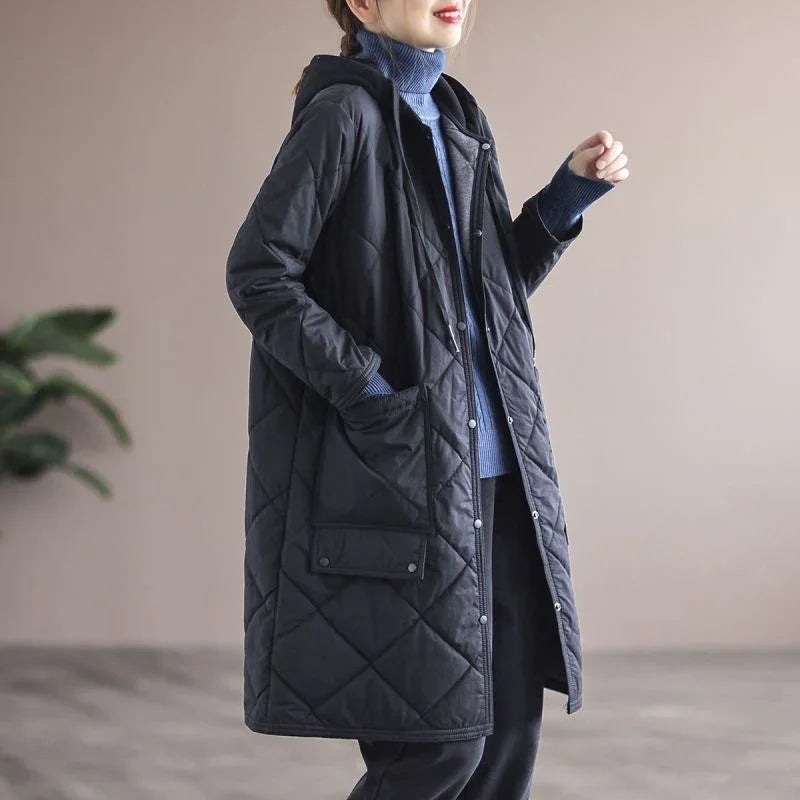 Woman wearing long black quilted hooded coat with large pockets, styled with blue turtleneck sweater
