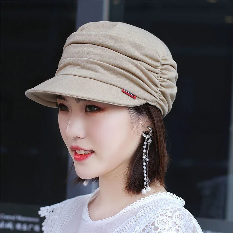 Woman wearing beige ruched newsboy cap and long pearl dangling earrings against dark background