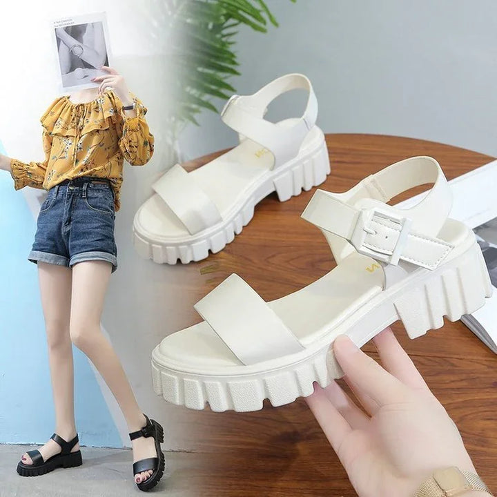 Chunky sole white platform sandals with ankle straps and adjustable buckles held by hand on wooden table