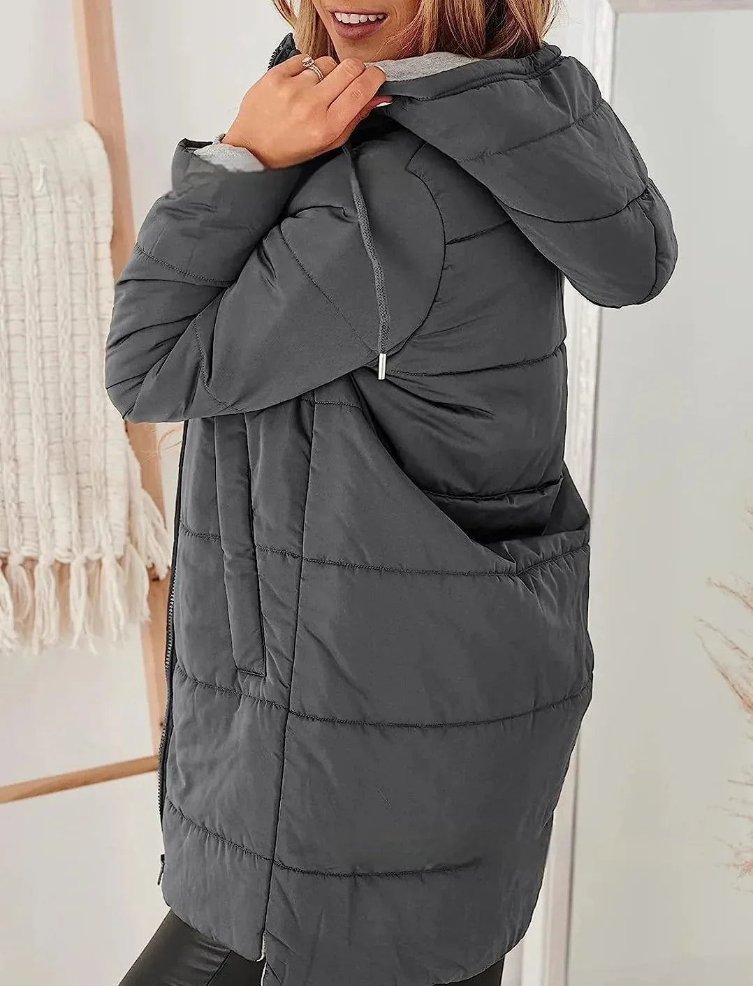 Woman wearing a dark gray hooded puffer jacket indoors with cozy decor background