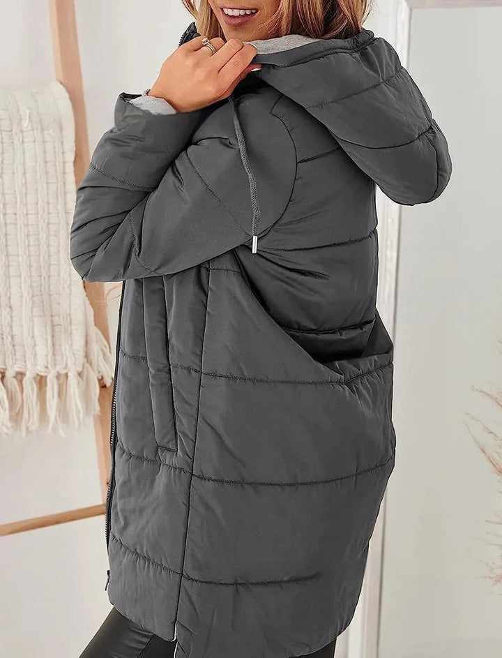 Woman wearing a dark gray hooded puffer jacket indoors with cozy decor background