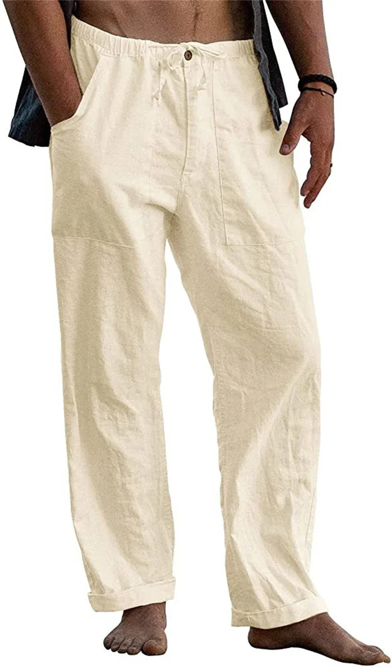 Man wearing beige casual drawstring pants with button and rolled cuffs, hands in pockets, barefoot