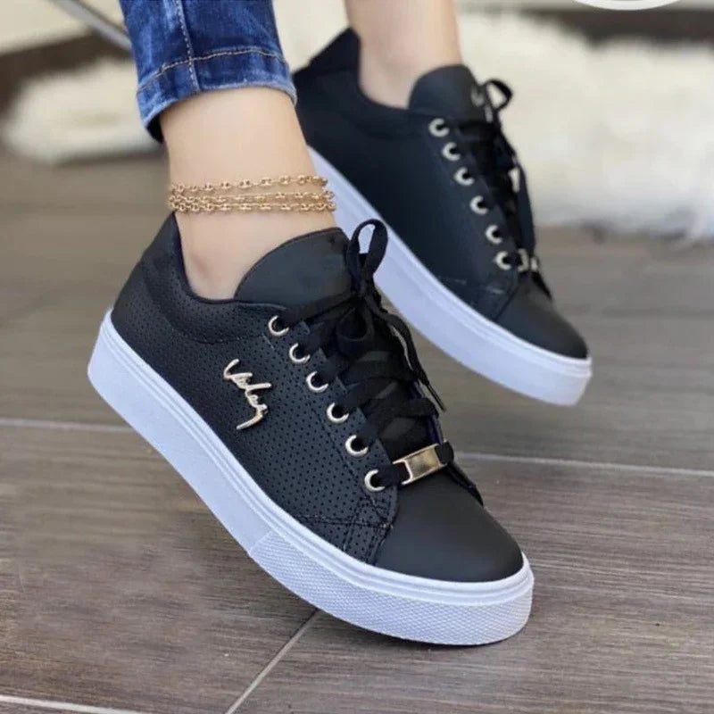 Black perforated casual sneakers with white thick soles and black laces worn with blue jeans and a gold anklet