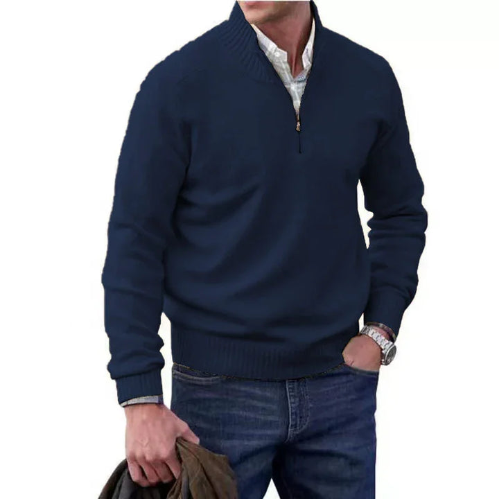 Man wearing navy blue quarter-zip sweater and jeans, holding brown jacket in hand