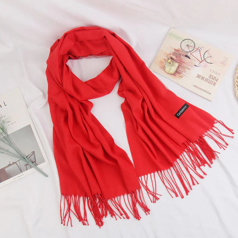 Bright red cashmere scarf with fringes displayed on white fabric background with magazines