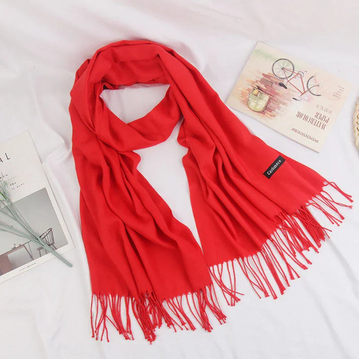 Bright red cashmere scarf with fringes displayed on white fabric background with magazines