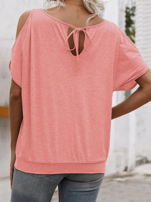 Back view of woman wearing a coral pink cold shoulder top with tie detail and casual blue jeans