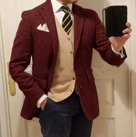 Man wearing a burgundy blazer, beige buttoned vest, striped black and yellow tie, and navy pants taking a mirror selfie