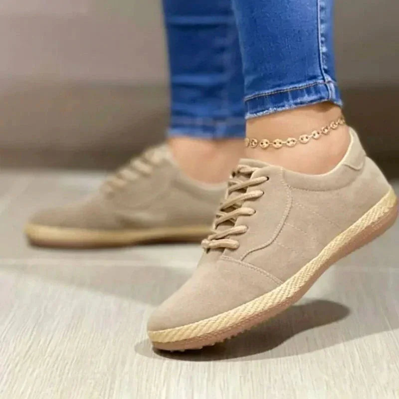 Beige casual lace-up sneakers with jute sole worn with blue skinny jeans and gold anklet on light floor