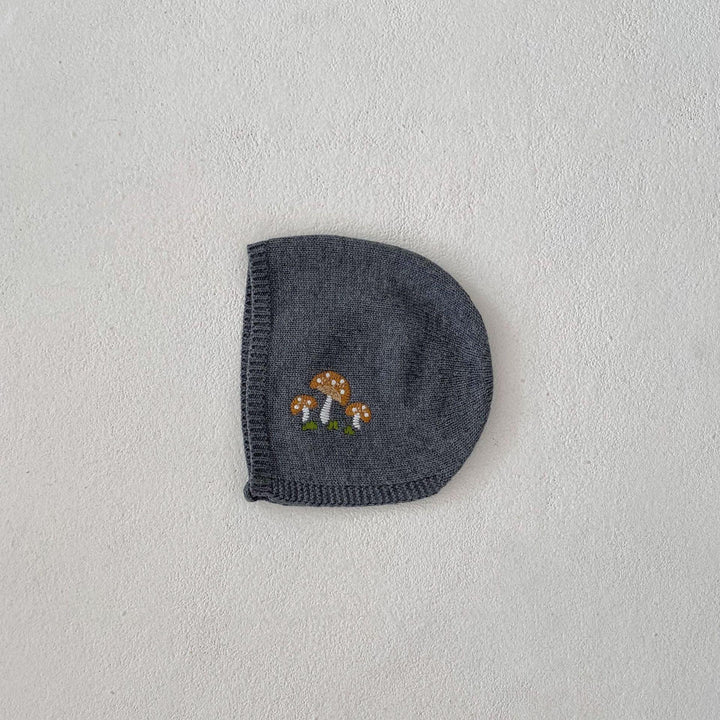 Gray knitted beanie with embroidered orange and white mushrooms on textured white surface