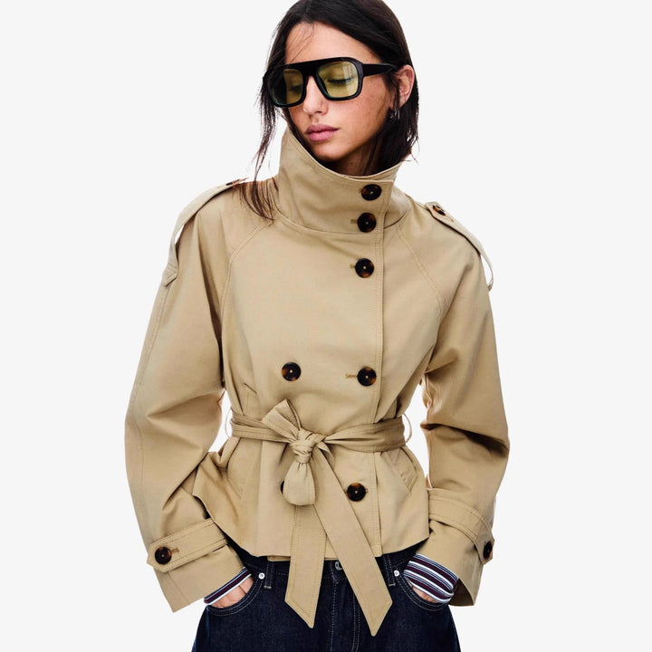 Woman wearing beige belted trench coat with high collar and oversized sunglasses