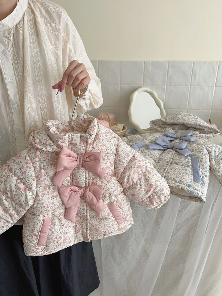 Woman holding a padded floral baby jacket with pink bows, with a second blue floral jacket on a table