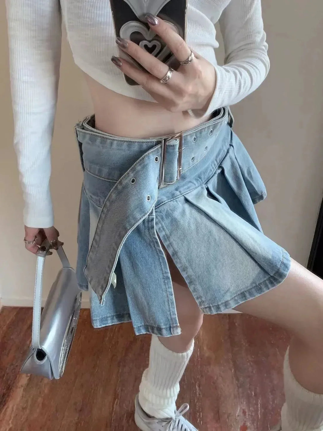 Fashion selfie of person in white top, belted denim skirt with slit, white socks, sneakers, and silver handbag