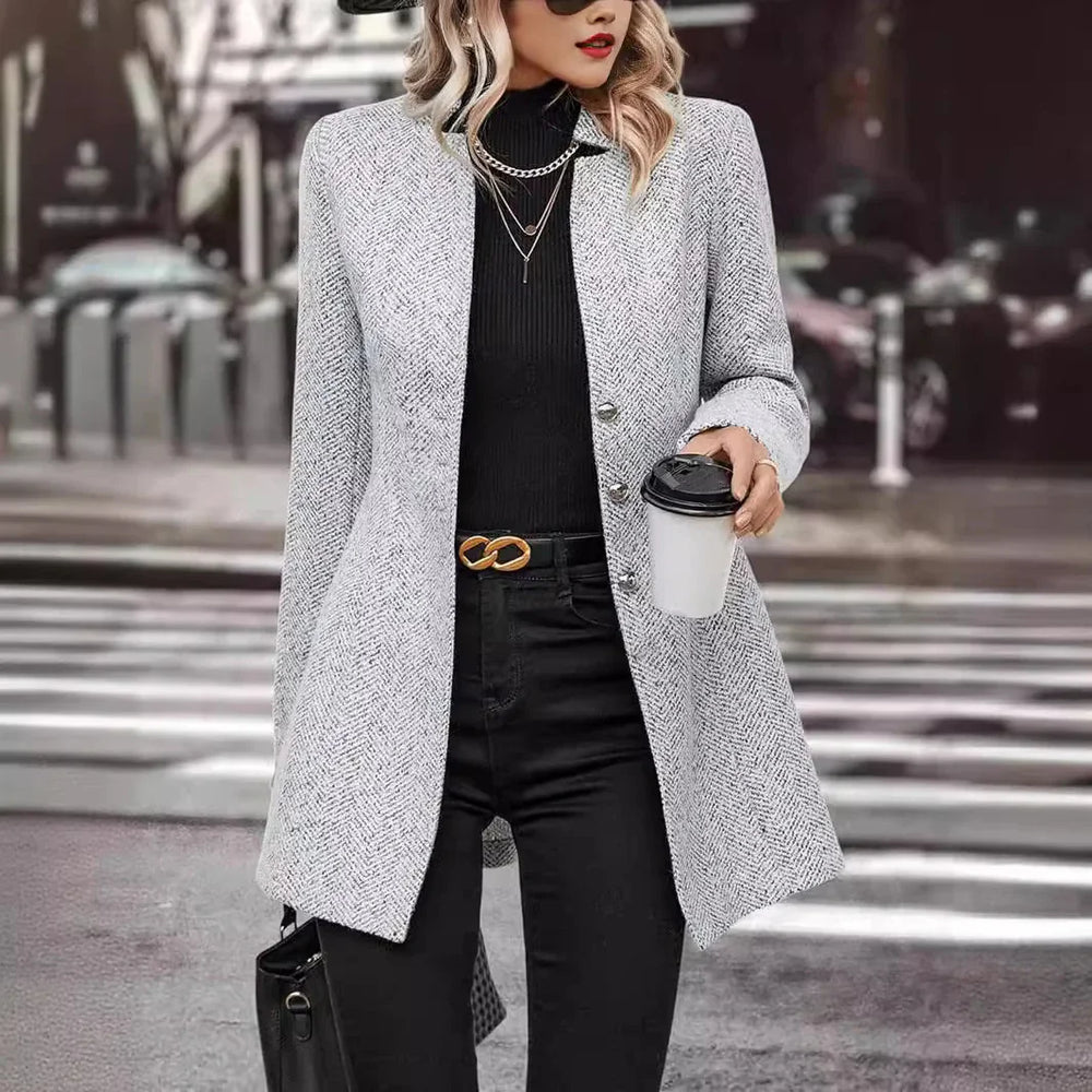 Woman in gray herringbone blazer with black turtleneck and pants holding coffee in urban street setting