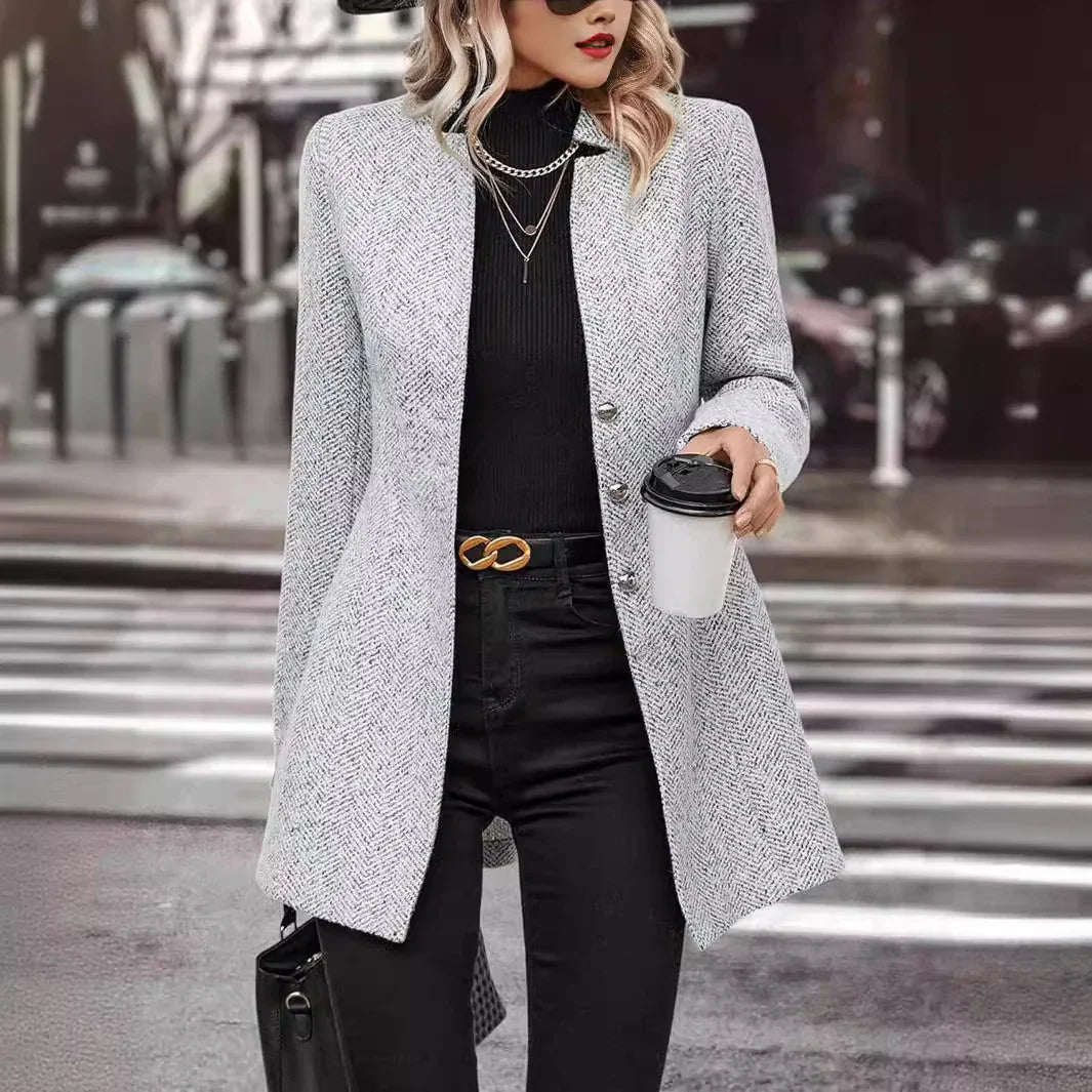 Woman in gray herringbone blazer with black turtleneck and pants holding coffee in urban street setting