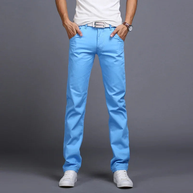Man wearing bright blue casual pants with white sneakers, a white belt, and a white t-shirt on gray background