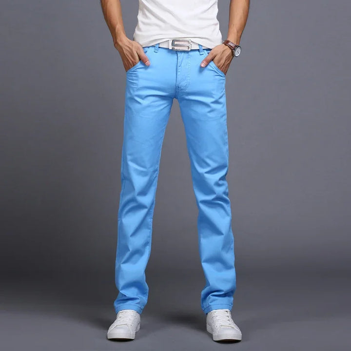 Man wearing bright blue casual pants with white sneakers, a white belt, and a white t-shirt on gray background