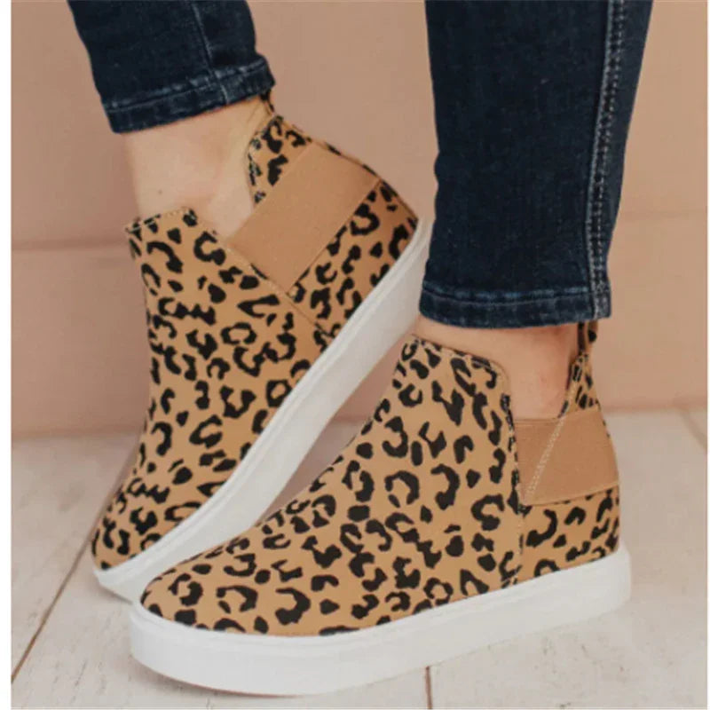 Leopard print slip-on wedge sneakers with white soles worn with dark jeans on wooden floor