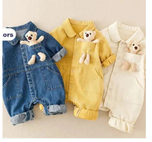 Three baby rompers in denim blue, mustard yellow, and cream with teddy bear in chest pocket