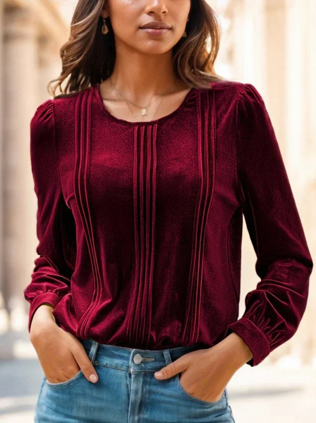 Woman wearing a burgundy velvet blouse with vertical pleats and long sleeves, paired with blue jeans