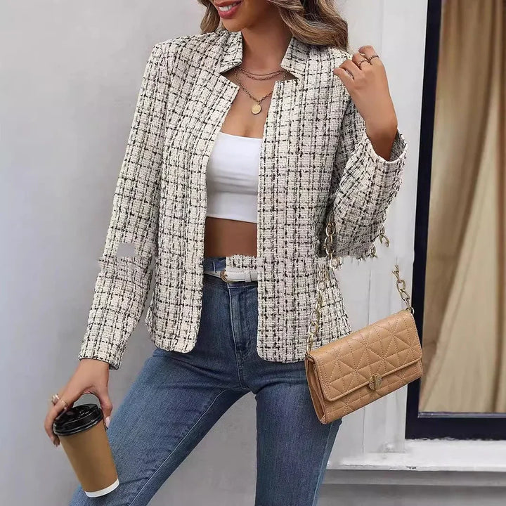 Woman wearing a plaid tweed blazer, white crop top, blue jeans, holding coffee cup, and tan quilted handbag